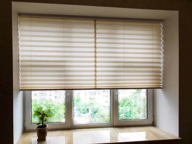 A cream pleated cellular shade lowered part way over a double window with a marble sill