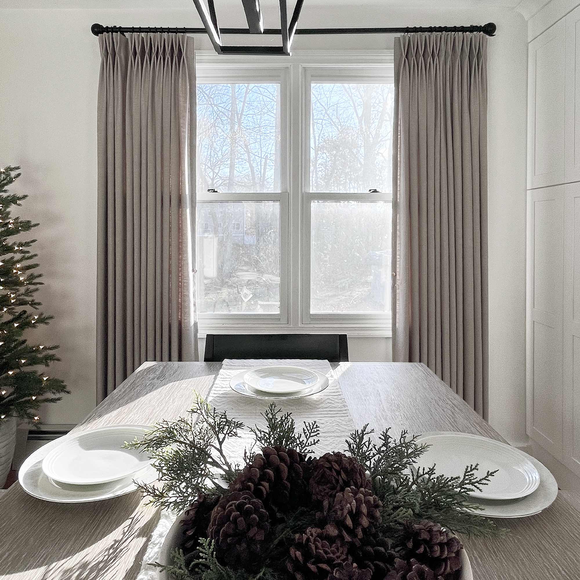 Taupe pinch pleat curtains on a black rod either side of a dining room window