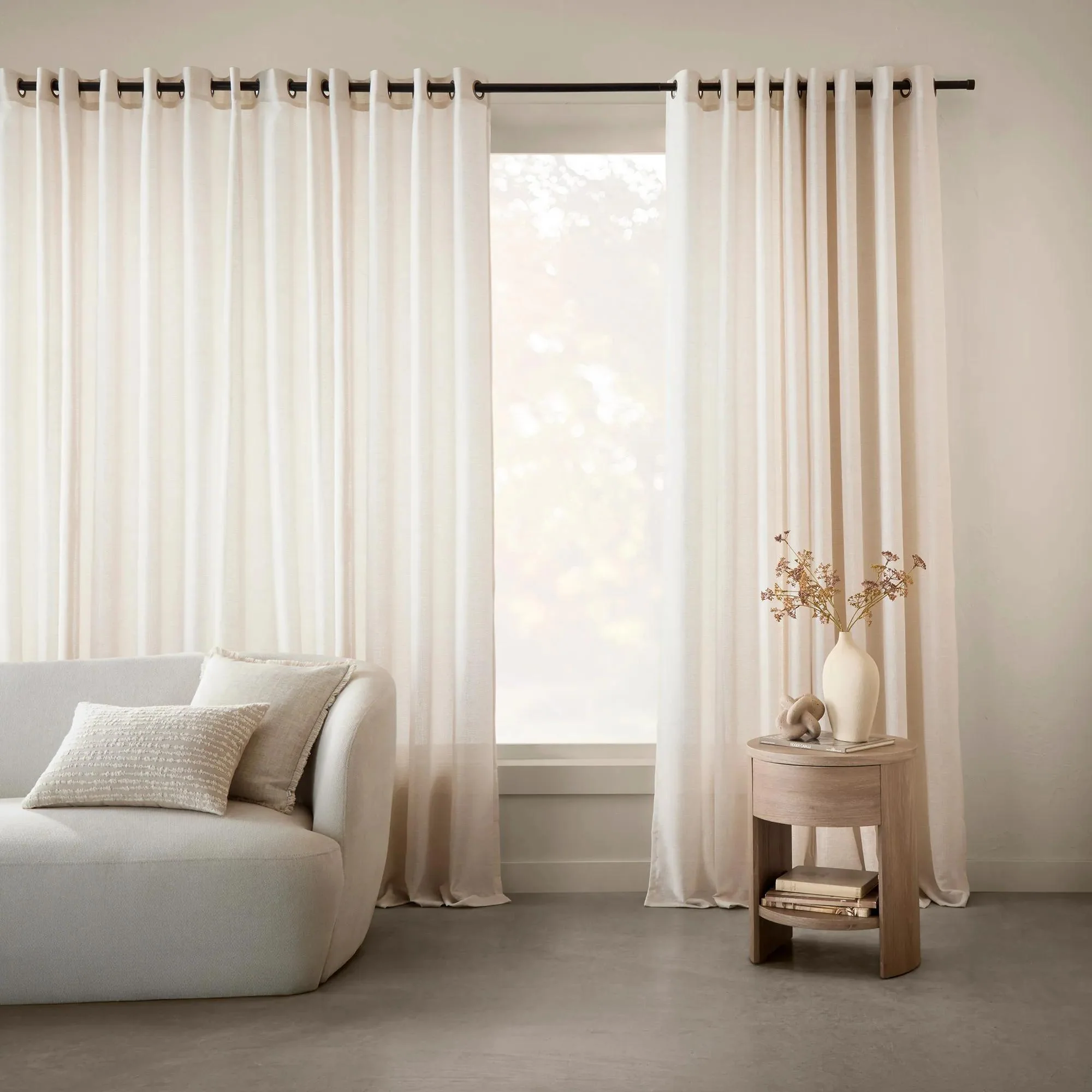 Cream grommet curtains on a black rod either side of a tall window