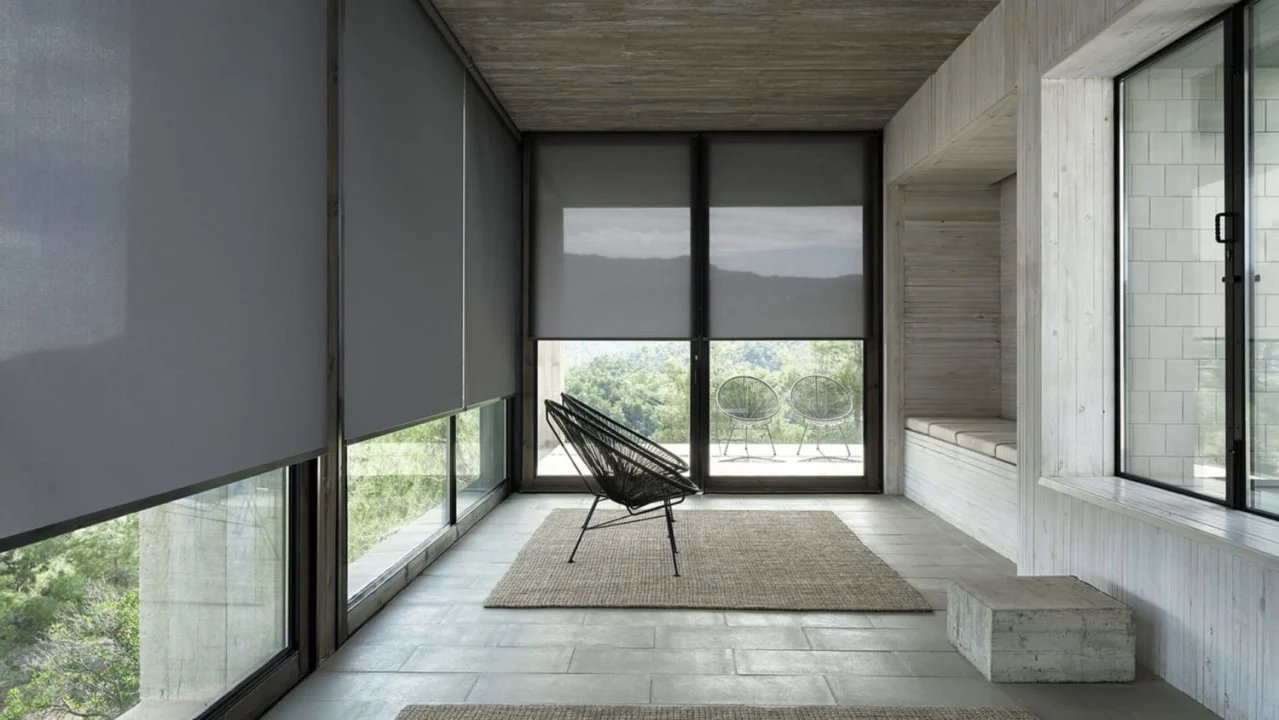 Charcoal solar roller shades in a concrete room opening onto a terrace and hills
