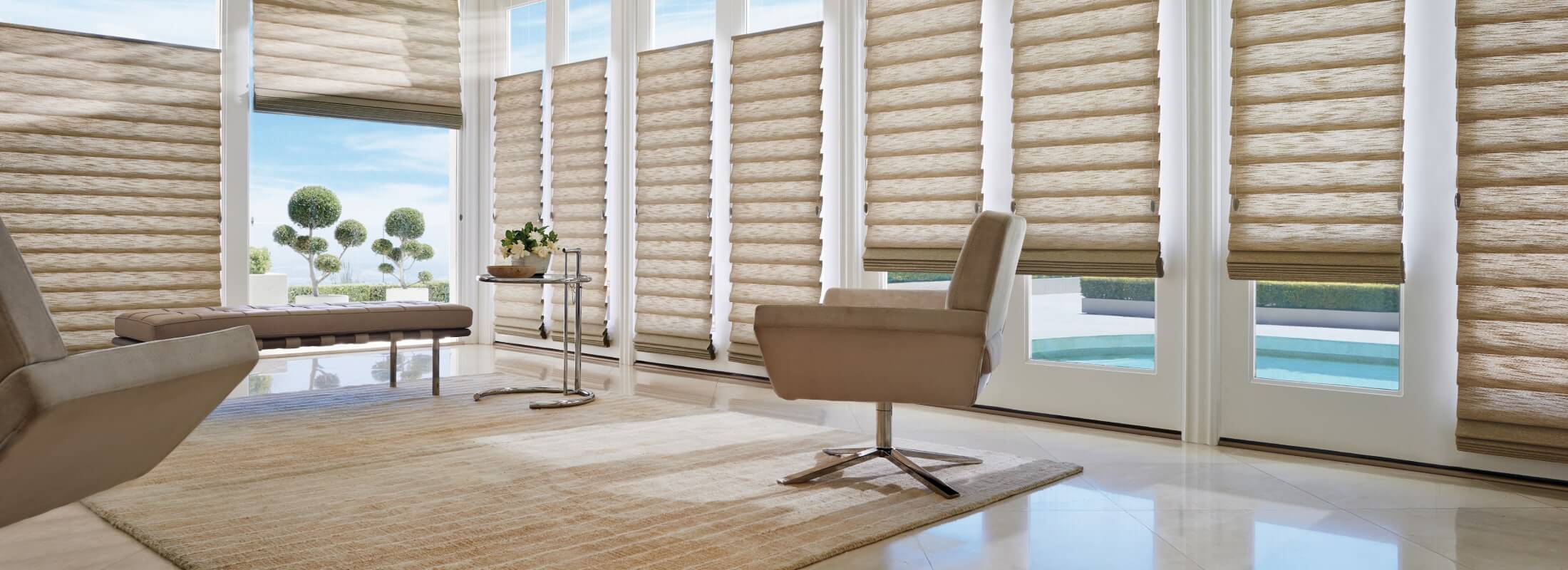 Sand coloured roman shades along a wall of glass doors opening to a pool terrace