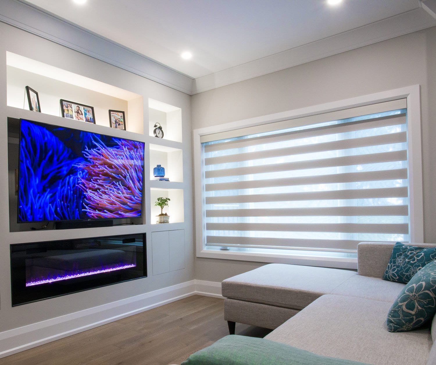 Grey zebra shades on a wide window in a family room, the bands set open beside a built in television wall