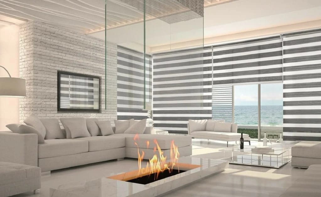 Grey and white zebra shades across a wall of glass in a bright living room, the sea beyond